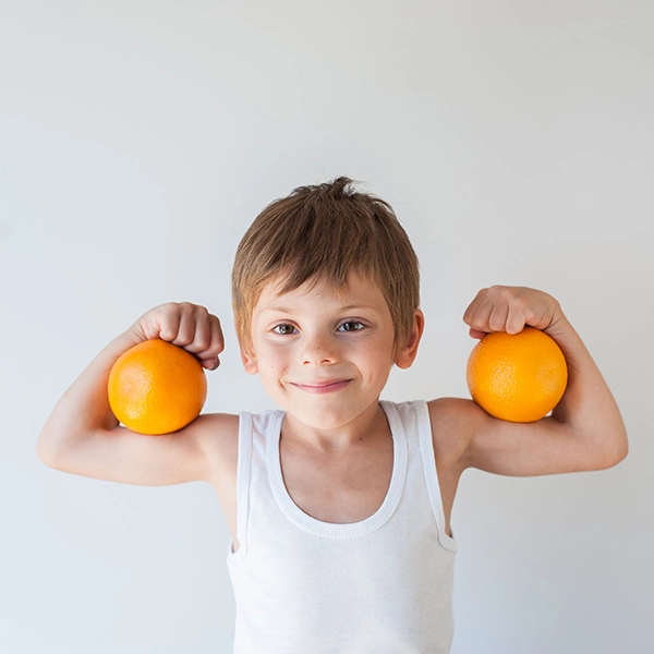 Das Kind zeigt Muskeln und hat gesunde Orangen in den Armen